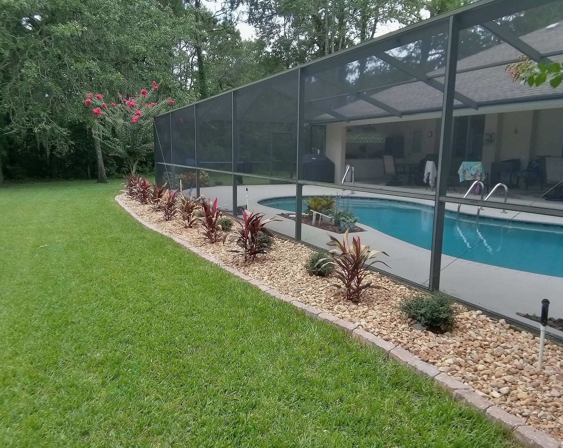 Paver wall along rock bed for plants along pool enclosure